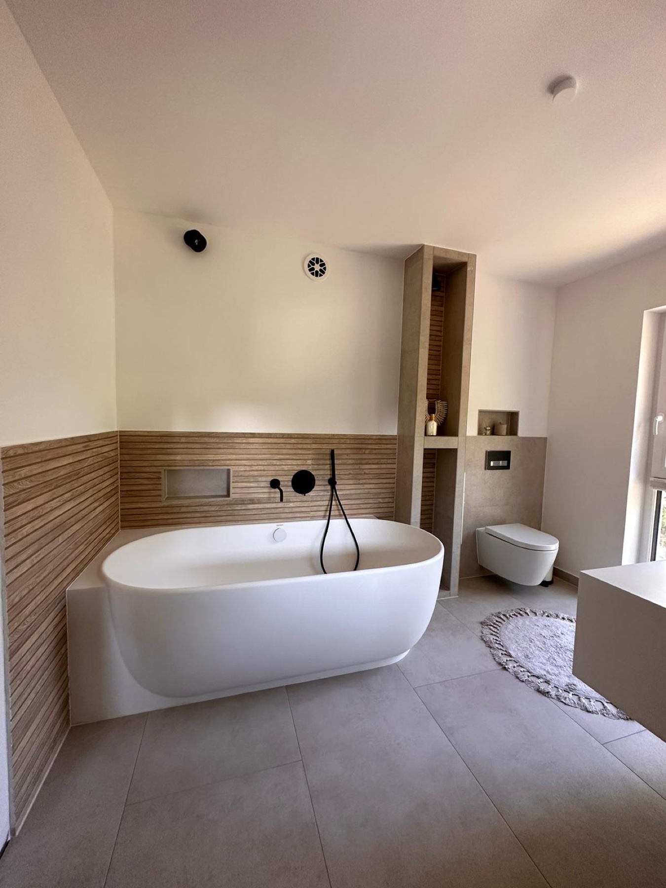 Ausgeführtes Bad mit freistehender weißer Wanne, grauem Fliesenboden und warmer Wandgestaltung