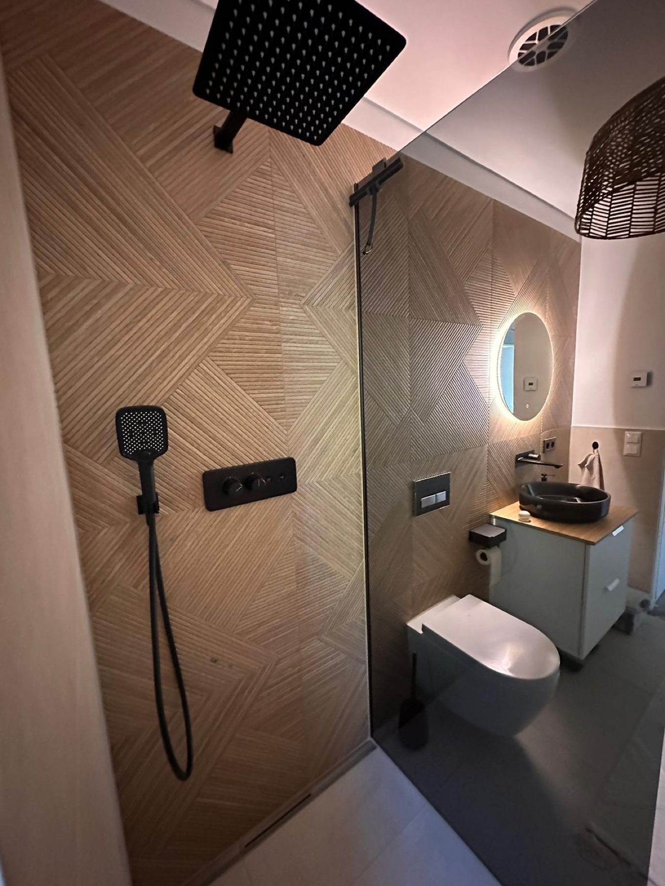 Dusche mit Holzoptikfliesen im Fischgrätmuster und schwarzer Kopfbrause